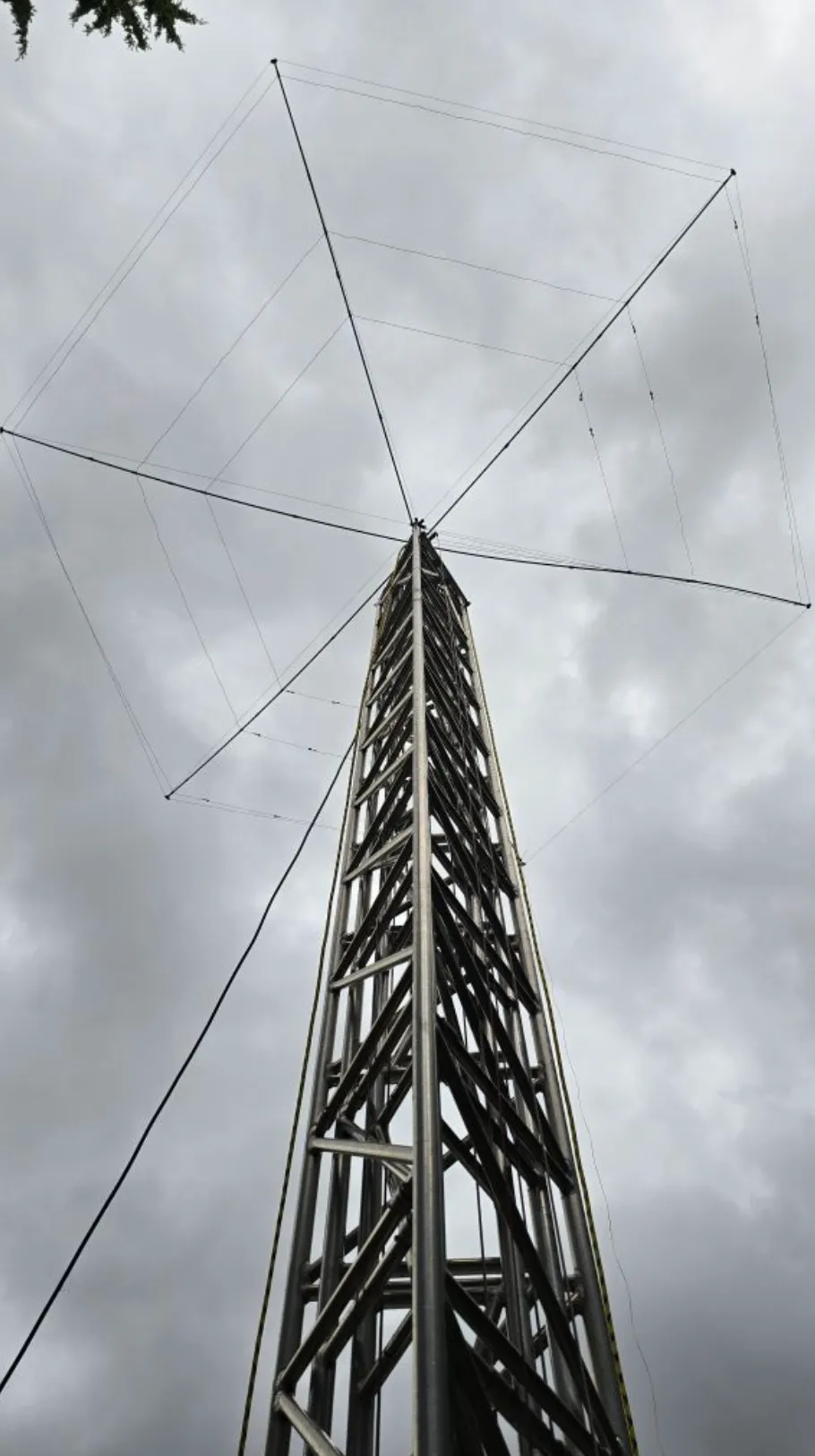 Looking up the N7OS HF tower — a lattice mast carrying the BuddiHex beam, its wire elements strung out against an overcast sky.